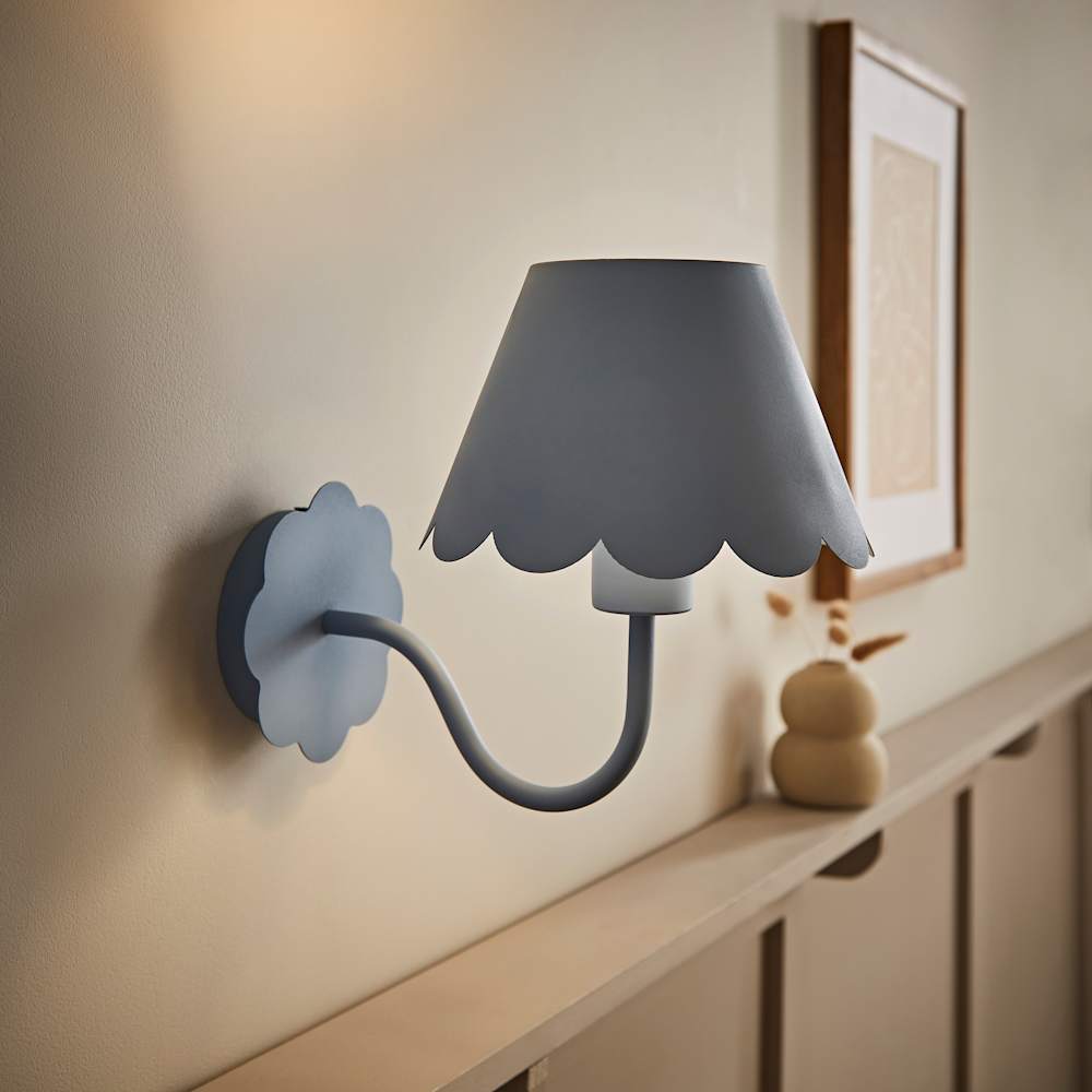 Powder blue scalloped wall sconce with curved arm and floral backplate mounted on white wall