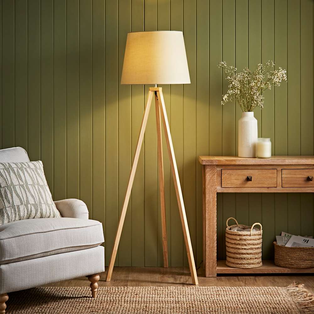 Scandinavian style living room corner with tripod floor lamp, wooden console table, vase with flowers, and olive green panelled wall