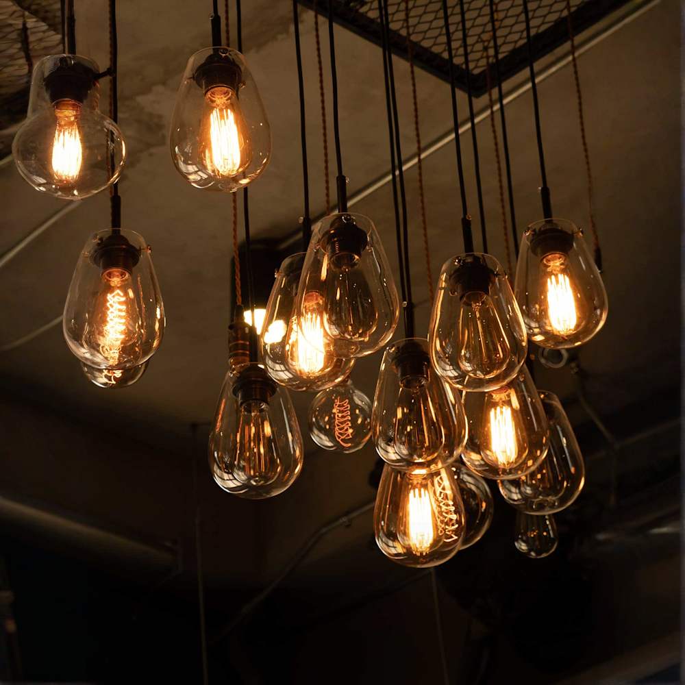A group shot of LED filament effect exposed bulbs suspended from black cables that are attached to an industrial looking grate