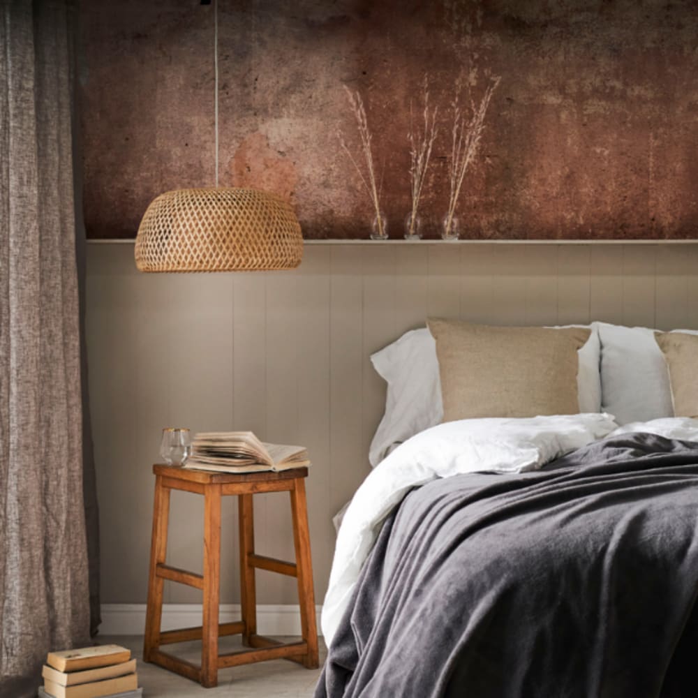 Scandi hygge bedroom with natural rattan woven pendant light, textured rust feature wall, neutral linen bedding and wooden bedside table