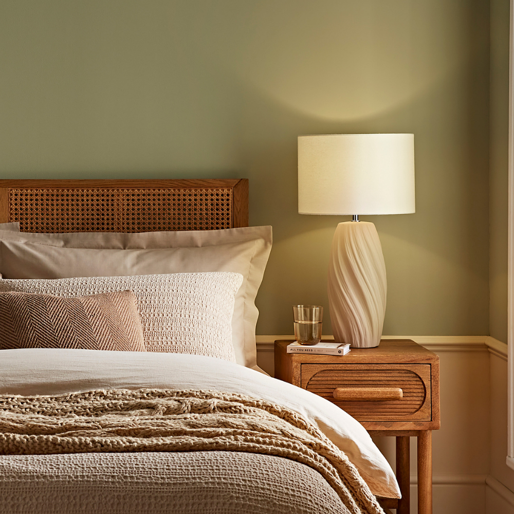 Warm neutral bedroom with rattan headboard and cream ceramic table lamp on wooden bedside table