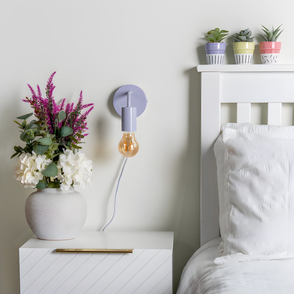 Modern bedroom with lilac wall light and exposed bulb beside white headboard and floral bedside décor