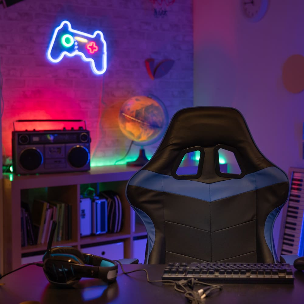 Modern gaming setup featuring a black and blue gaming chair, RGB neon controller wall light, keyboard, and headset on desk in a colourful LED-lit room.
