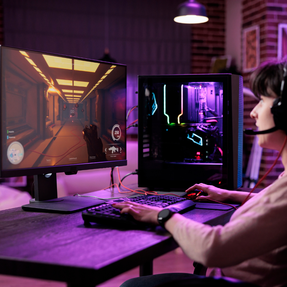Woman gaming on a PC with RGB lights, wearing a headset and playing a first-person shooter game on a large monitor in a modern gaming room.