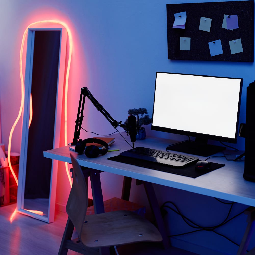 Gaming and streaming desk setup featuring a red LED rope strip light around a mirror, microphone arm, headset, and monitor in a blue ambient-lit room.