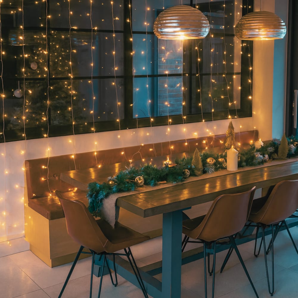 Modern dining room decorated for Christmas with fairy lights, garland, candles, and warm festive accents, creating a cosy evening glow