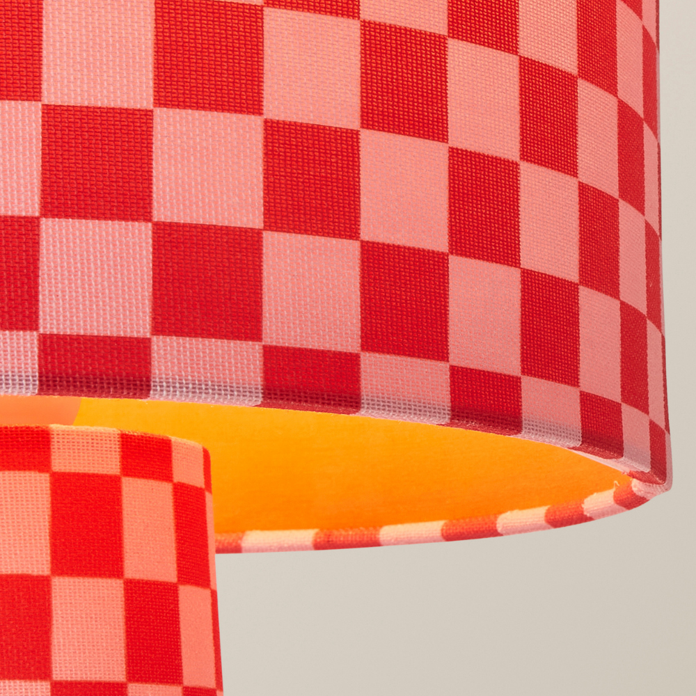 Red and pink checkerboard table lamp with a colour‑matched shade inner glowing warmly.