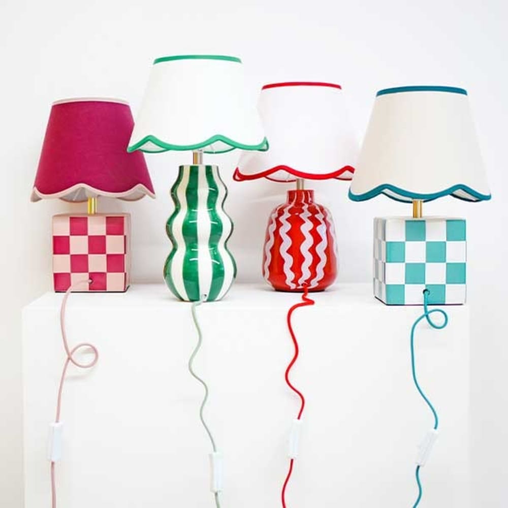A set of four decorative table lamps displayed on a white surface. Each lamp has a patterned base and a scalloped lampshade with matching trim. All lamps have colour coordinated power cords.