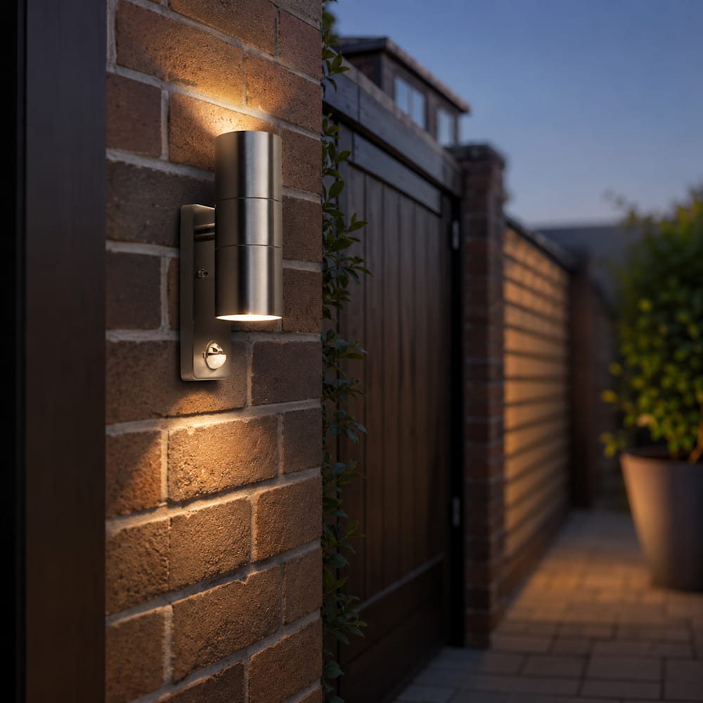 Stainless steel PIR wall light mounted on a brick wall beside a wooden side gate, casting a downward beam of light onto the brickwork.