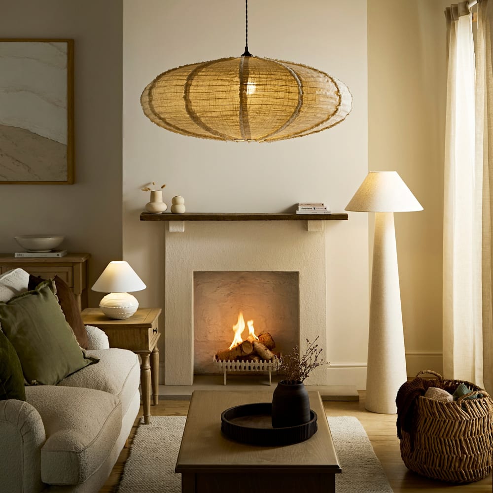 Warm modern rustic living room with cream sofa, olive cushions, wood coffee table, fireplace, woven pendant light, floor lamp, wicker basket, and linen curtains over bright French doors.